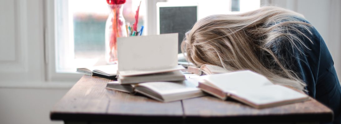 girl with head in books on desk